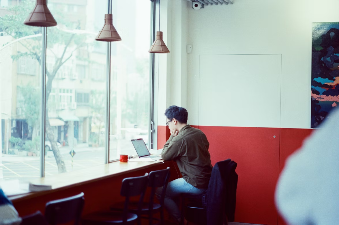 A person sitting alone in a cafe, working. Credits: Unsplash